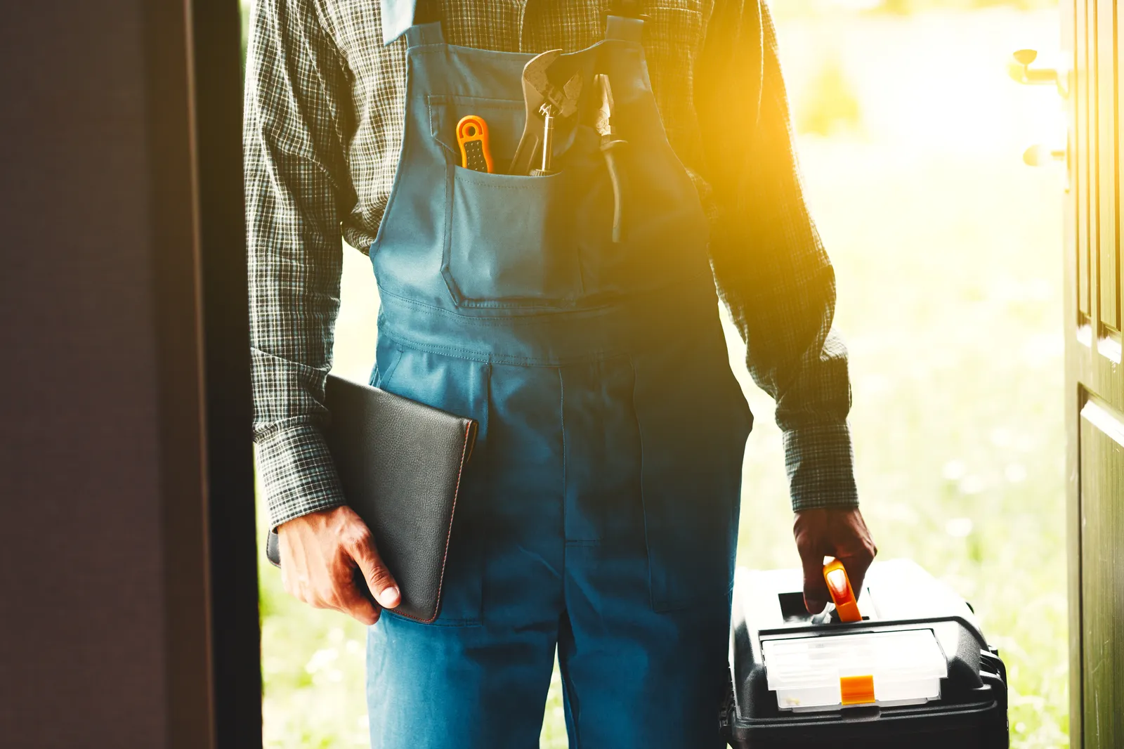 Field service technician with toolbox at sunlit doorway